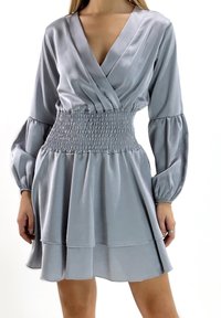 Grijze satijnen jurk met een diepe V-hals, een gerimpelde taille en lange, pofmouwen. De rok heeft gelaagde volants aan de zoom.