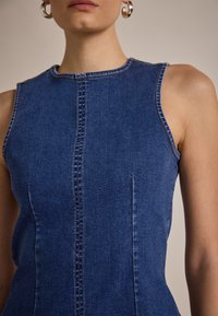 Rochie din denim fără mâneci, de culoare albastru închis, cu o formă ajustată, cusături vizibile și detalii pe cusăturile laterale. Textură netedă, design clasic.