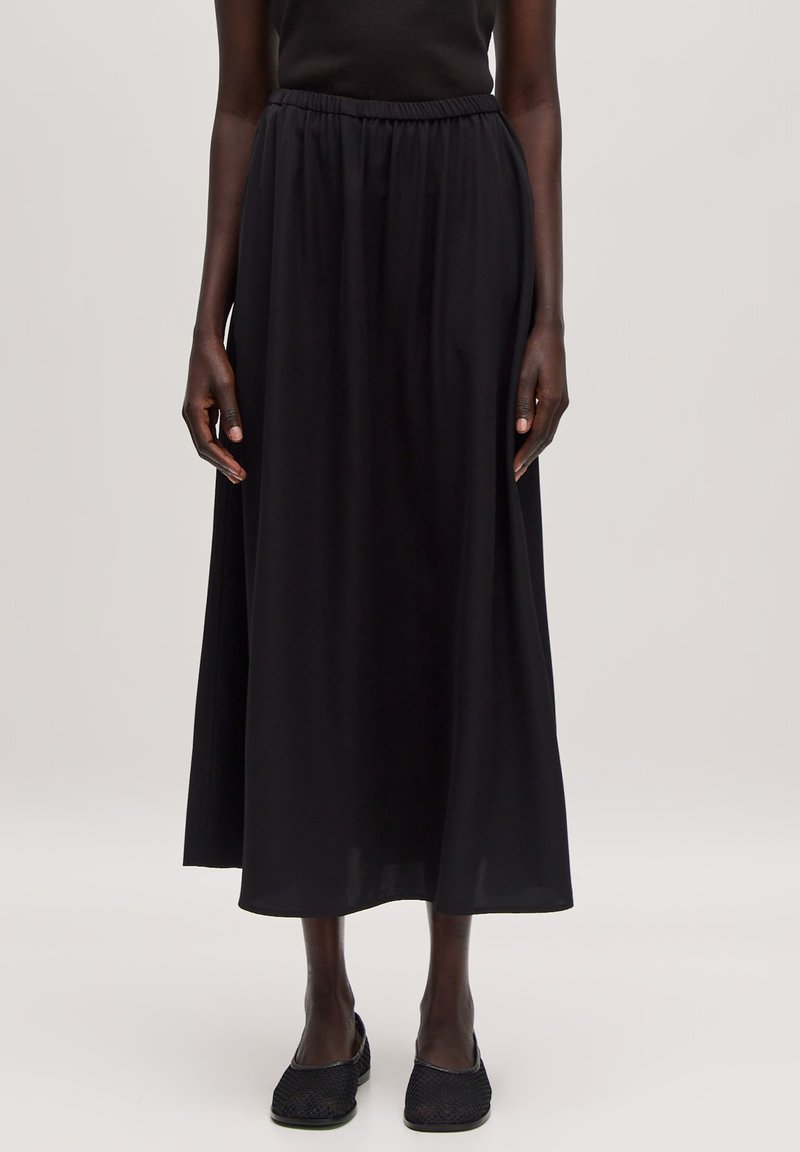 Zwarte maxi rok gemaakt van lichtgewicht stof met een elastische tailleband, vloeiende design en een gladde textuur. Vergezeld van zwarte geweven schoenen.