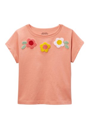 Haut court à manches courtes couleur pêche avec trois fleurs texturées en rose, jaune et blanc sur la poitrine, chacune accompagnée de feuilles vertes.