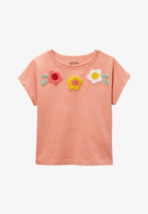 Haut court à manches courtes couleur pêche avec trois fleurs texturées en rose, jaune et blanc sur la poitrine, chacune accompagnée de feuilles vertes.