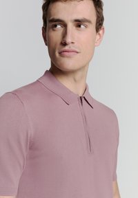 Polo met korte mouwen in een stoffige rozenkleur, vervaardigd uit een zachte, rekbare stof met een ritskraag en ribgebreide randen.