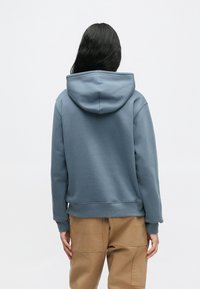 Φούτερ με κουκούλα σε μπλε-γκρι φλις, με άνετη εφαρμογή, ρεβέρ στο τελείωμα και μακριά μανίκια. Συνδυασμένο με καφέ cargo παντελόνια.