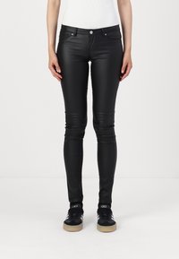 Black faux leather skinny pants with a smooth texture, front pockets, and a button closure, paired with black sneakers.