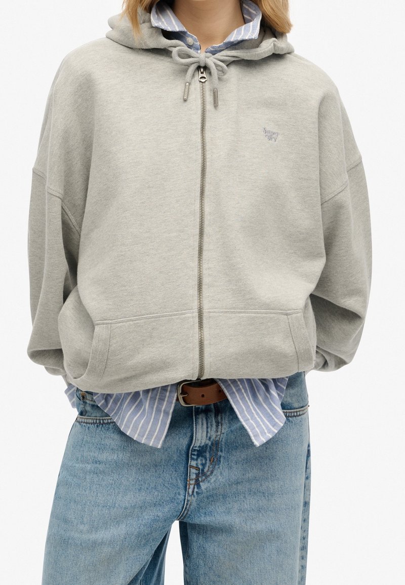 Felpa grigia in cotone con zip, cappuccio regolabile, dotata di cerniera frontale, tasche laterali e un piccolo logo sul petto.