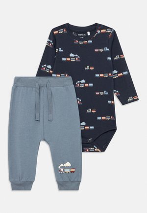 Marineblå babybody med lange ermer og fargerike togtprenter, kombinert med lyseblå bukser med snor og en liten tog-brodering.
