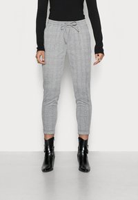 Grijs geruite broek met een elastische tailleband en een trekkoord. Aansluitend ontwerp met taps toelopende benen, gecombineerd met zwarte enkellaarsjes.