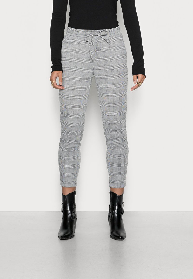 Grijs geruite broek met een elastische tailleband en een trekkoord. Aansluitend ontwerp met taps toelopende benen, gecombineerd met zwarte enkellaarsjes.