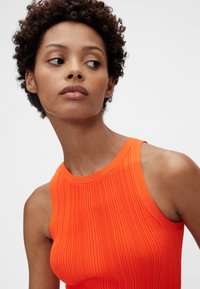 Orange ribbet tanktop med brede stropper, der har et tætsiddende design. Glat tekstur og en høj halsudskæring fremhæver dens moderne stil.