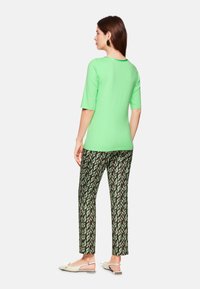 Mint green short-sleeve top paired with black and green patterned trousers. White slip-on shoes and circular earrings complete the look.