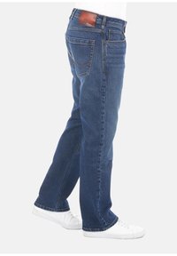 Jeans in denim di colore blu scuro con un design a gamba dritta, dotati di tasche posteriori e etichetta in pelle marrone sulla vita. Sneakers bianche completano il look.