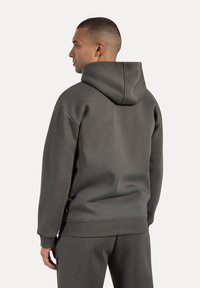 Sudadera con capucha en tejido gris oscuro con una textura suave. Presenta puños y dobladillo de canalé, con un corte relajado y un branding mínimo en el costado.