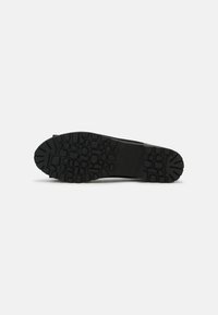 Semelle de chaussure noire avec un motif de bande de roulement robuste comprenant différentes formes rectangulaires et irrégulières pour l'adhérence et la durabilité.