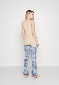 Top de tanque bege com um design ajustado, combinado com calças flare azuis tie-dye que apresentam uma textura suave e uma variação de cor subtil.