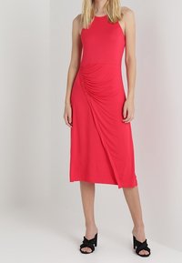 Vestito midi rosso realizzato in tessuto elasticizzato, con corpo aderente, arricciature laterali e orlo asimmetrico. Indossato con sandali neri con tacco.
