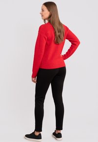 Roter Strickpullover mit lockerer Passform, gerippten Bündchen und Saum, kombiniert mit schwarzen Leggings und schwarzen Sneakern. Glatte Textur.