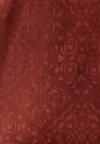 Strukturierter Stoff in einem tiefen Rostton mit einem subtilem Blumen- und geometrischen Muster. Die Oberfläche wirkt weich und leicht erhaben.
