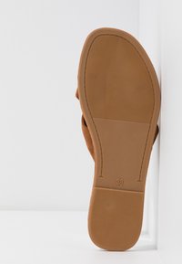 Semelle d'une sandale plate marron avec des zones de grip texturées et le numéro de taille 38 estampillé près du talon sur fond blanc.