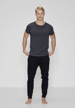 Mørkegrå tætsiddende t-shirt kombineret med sorte joggers, begge i blødt stof. Modellen står barfodet med hænderne i lommerne, neutralt baggrund.