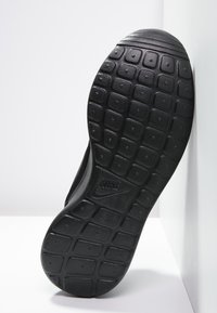 Svart atletisk skosula med en texturerad, mönstrad design. Utrustad med gummimaterial och en framträdande logotyp nära valvet.