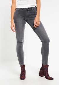 Jeans skinny grigi con una texture liscia, dotati di cinque tasche e vita a media altezza, abbinati a stivali alla caviglia a fantasia in rosso scuro e blu.