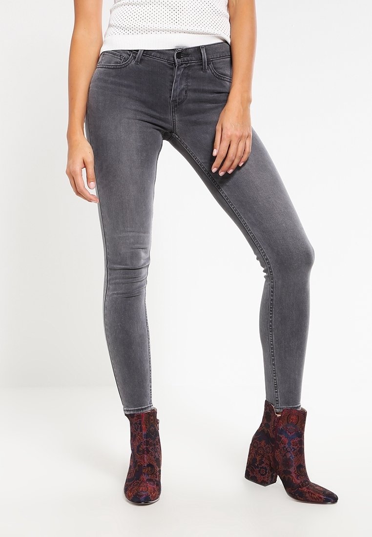 Jeans skinny grigi con una texture liscia, dotati di cinque tasche e vita a media altezza, abbinati a stivali alla caviglia a fantasia in rosso scuro e blu.