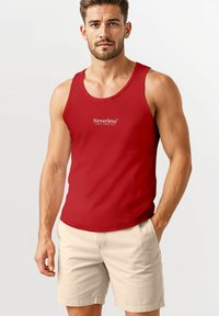 Rotes Tanktop aus Baumwolle mit Rundhalsausschnitt und Logo-Text. Kombiniert mit hellbeigen Shorts, die einen lässigen Sommerlook präsentieren.