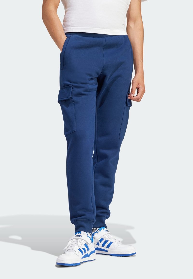 Navy blue cargo joggers made of soft cotton blend, featuring side pockets and a ribbed waistband, paired with white sneakers with blue accents.