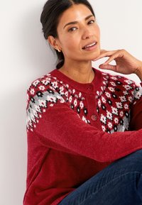 Roter gestrickter Pullover mit einem gemusterten Einsatz in Schwarz, Weiß und Rot. Hat einen runden Ausschnitt und zwei Knöpfe an der Vorderseite. Weiche Textur.