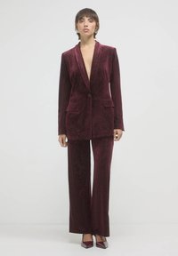 Completo in velluto bordeaux con blazer a un bottone, revers dritto e pantaloni a gamba larga caratterizzati da una sottile texture scintillante.