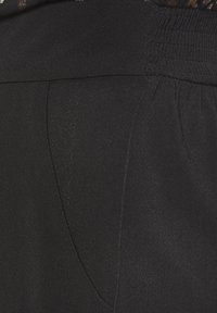 Melni bikses ar elastīgu jostasvietu, gludu auduma tekstūru un diagonālām sānu kabatām. Nav redzamu rakstu vai akcentu.