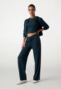 Dark teal lounge set featuring a cropped top and loose-fitting trousers. Soft fabric texture with a zip-up jacket and drawstring waistband.