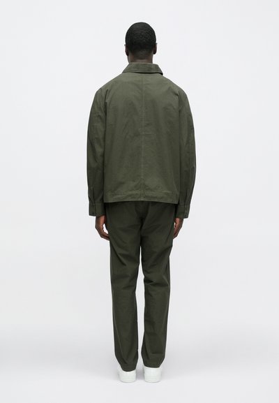 Olívovo zelená bavlnená bunda s golierom, doplnená o zladené nohavice. Oblečenie má voľný strih a hladkú textúru, zobrazené zozadu.