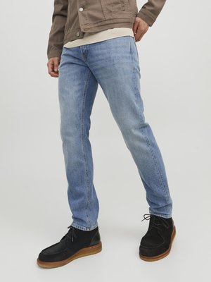 Jeans en denim bleu clair avec une coupe droite, associés à des bottes en suède noires. La tenue présente un look décontracté en couches avec une veste marron.