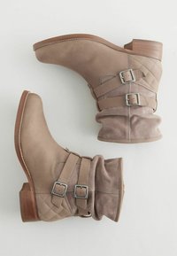 Bottines en cuir beige avec des accents en daim matelassé, deux boucles ajustables sur le côté et un talon en bois empilé.