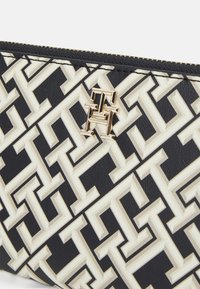 Pochette a motivi neri e crema con design geometrico, caratterizzata da un dettaglio del logo in tonalità dorata e chiusura con zip. Realizzata in materiale sintetico testurizzato.