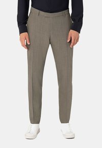 Maßgeschneiderte beige Hosen mit einer strukturierten Oberfläche, schmalem Schnitt, zwei Vorderaschen und Gürtelschlaufen, kombiniert mit weißen Sneakers.