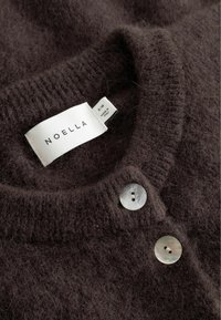 Brązowy sweter z dzianiny o miękkiej, puszystej fakturze. Posiada prążkowany kołnierz oraz dwa duże, okrągłe guziki z masy perłowej. Widoczna etykieta marki.
