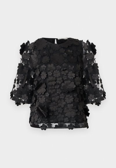 Sort blomstret applikation top med gennemsigtige ærmer, der har tredimensionelle blomsterdetaljer og en rund halsudskæring. Inkluderer en nøglehulslukning i ryggen.