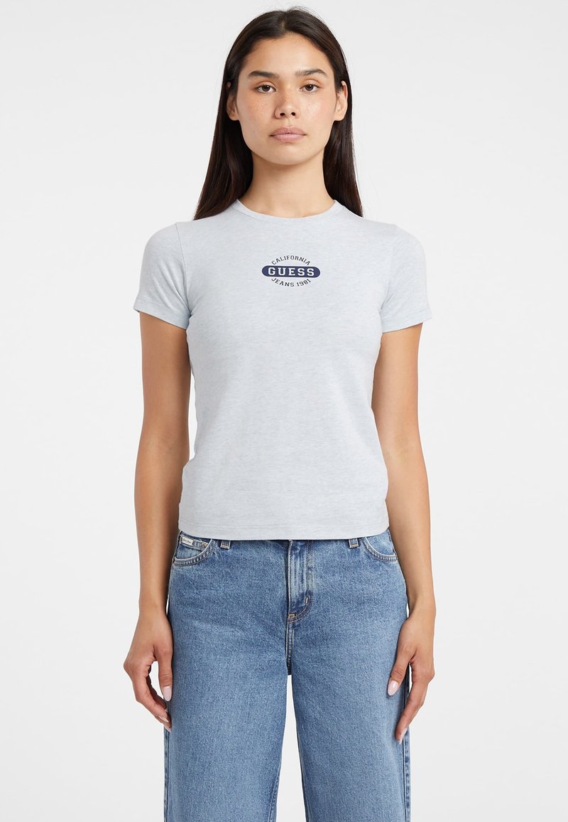 Jasnoszara, dopasowana koszulka z bawełny z centralnym granatowym logo, na którym widnieje napis "CALIFORNIA GUESS JEANS 1981". Krótkie rękawy.