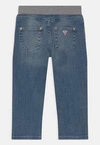 Pantalones vaqueros con cintura elástica gris, con dos bolsillos traseros y un pequeño emblema de logo en el bolsillo izquierdo. Color azul medio.