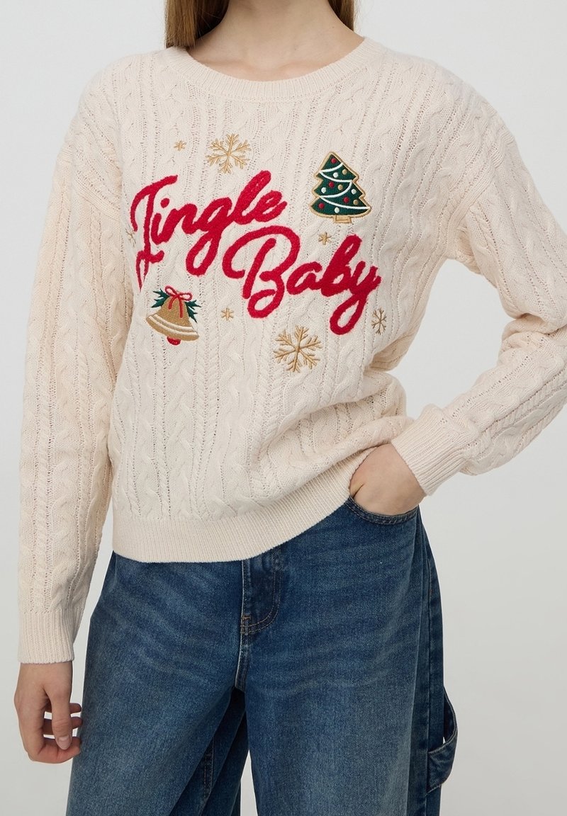 Pull en maille crème avec texte rouge « Jingle Baby », décoré d'une cloche brodée, d'un sapin de Noël et de flocons d'or.