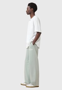 Hvid bomulds t-shirt i afslappet pasform. Lys grøn brede sweatpants med blød tekstur og logo detalje. Modellen har hvide sneakers på.