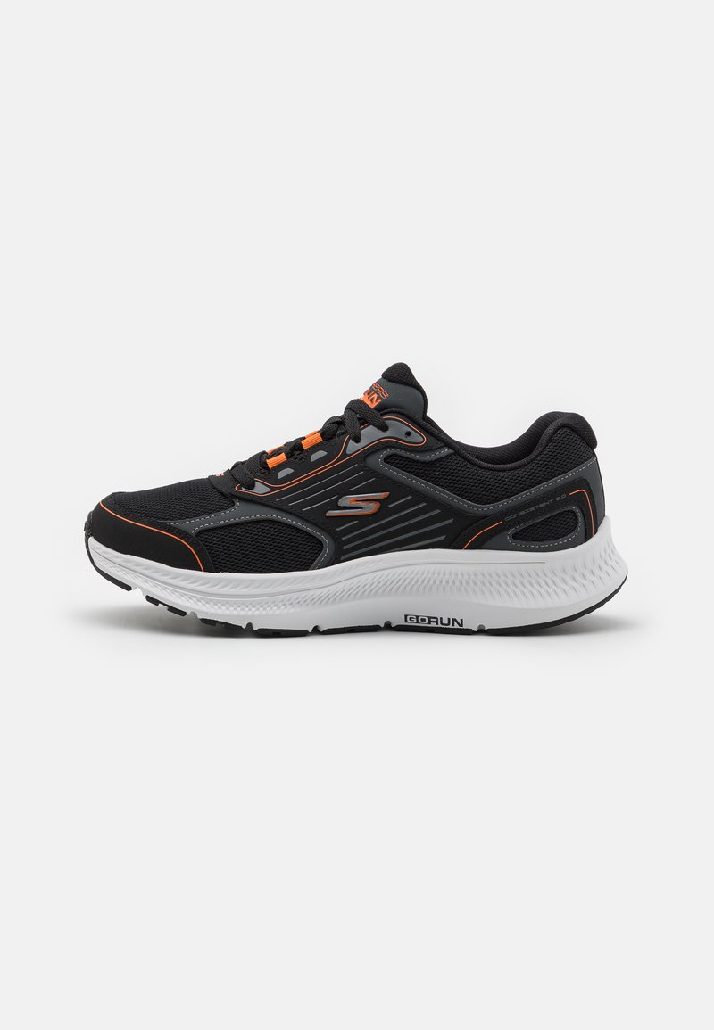 Zapatilla deportiva negra con parte superior de malla y acentos naranjas, una mediasuela blanca acolchada y una suela de goma texturizada para mayor agarre.