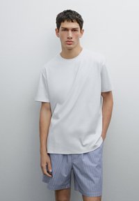 T-shirt bianca in cotone con maniche corte abbinata a pantaloni corti a righe blu e bianche, che mostra un aspetto casual e una texture liscia.
