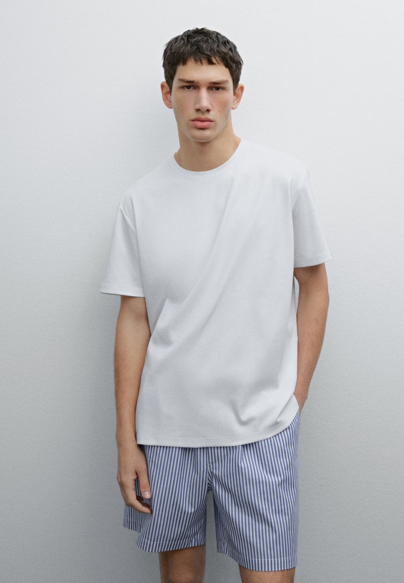 T-shirt bianca in cotone con maniche corte abbinata a pantaloni corti a righe blu e bianche, che mostra un aspetto casual e una texture liscia.