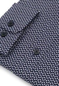 Granatowa koszula z białym i jasnoniebieskim wzorem kwiatowym, z czarnymi guzikami i złożonym mankietem.