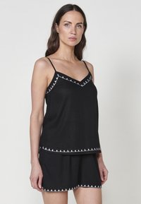 Musthave musta lühikeste varrukateta topp ja lühikesed püksid, mis on valmistatud pehmest kangast. Kerge valge tikand kaunistab kaelaauku ja alläärt.