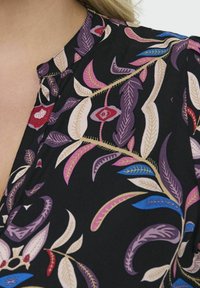 Top in tessuto nero con vivaci motivi di foglie nei colori viola, rosa, rosso e blu, dotato di colletto con bottoni e una texture liscia.