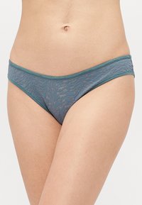 Tengeri zöld csipkebikini alsó, virágos mintával, széles gumis derékkal, puha textúrával és minimális takarással. 